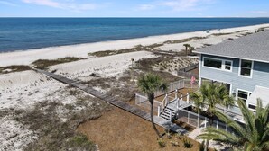 Una casa de playa con terraza de madera, una pequeña escalera y vista al océano.