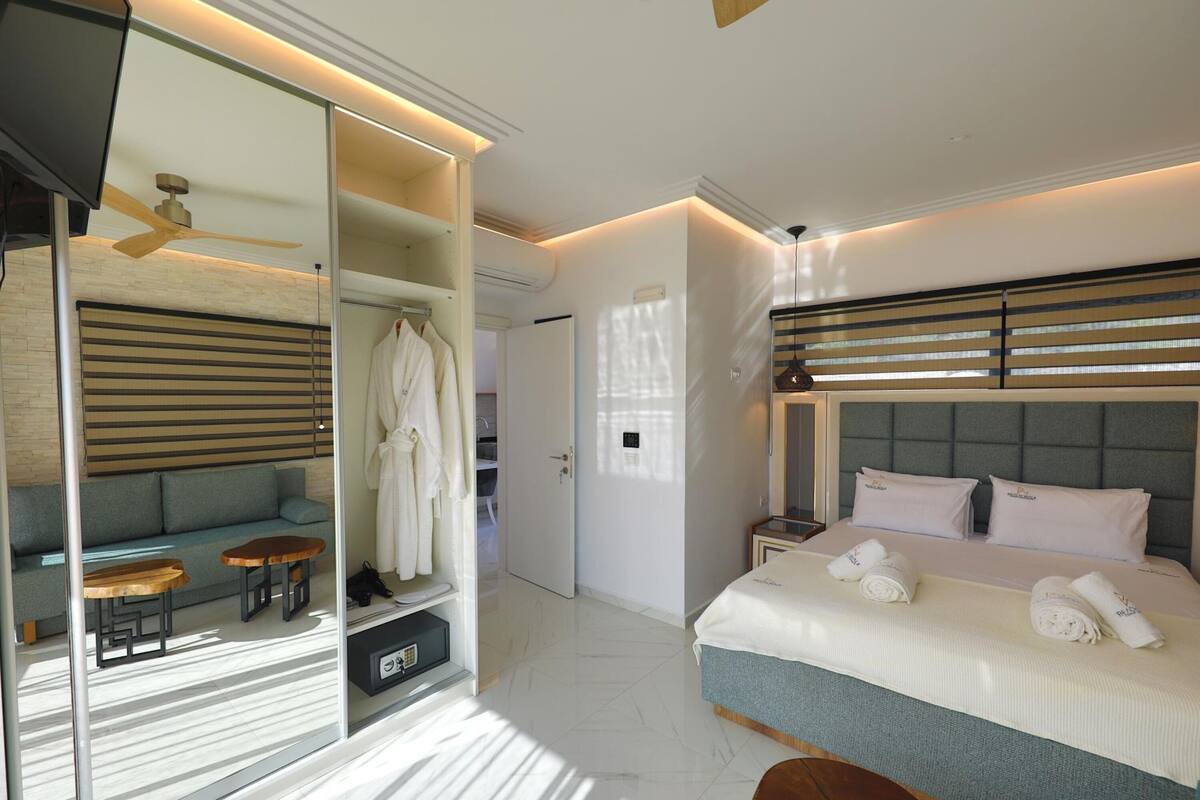 A modern hotel room with a bed, a seating area with a sofa and small tables, a wardrobe, and a ceiling fan.