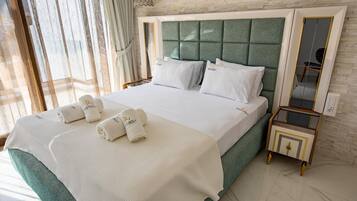 A neatly made bed with white linens and towels, a green upholstered headboard, and a small bedside table with a mirror.