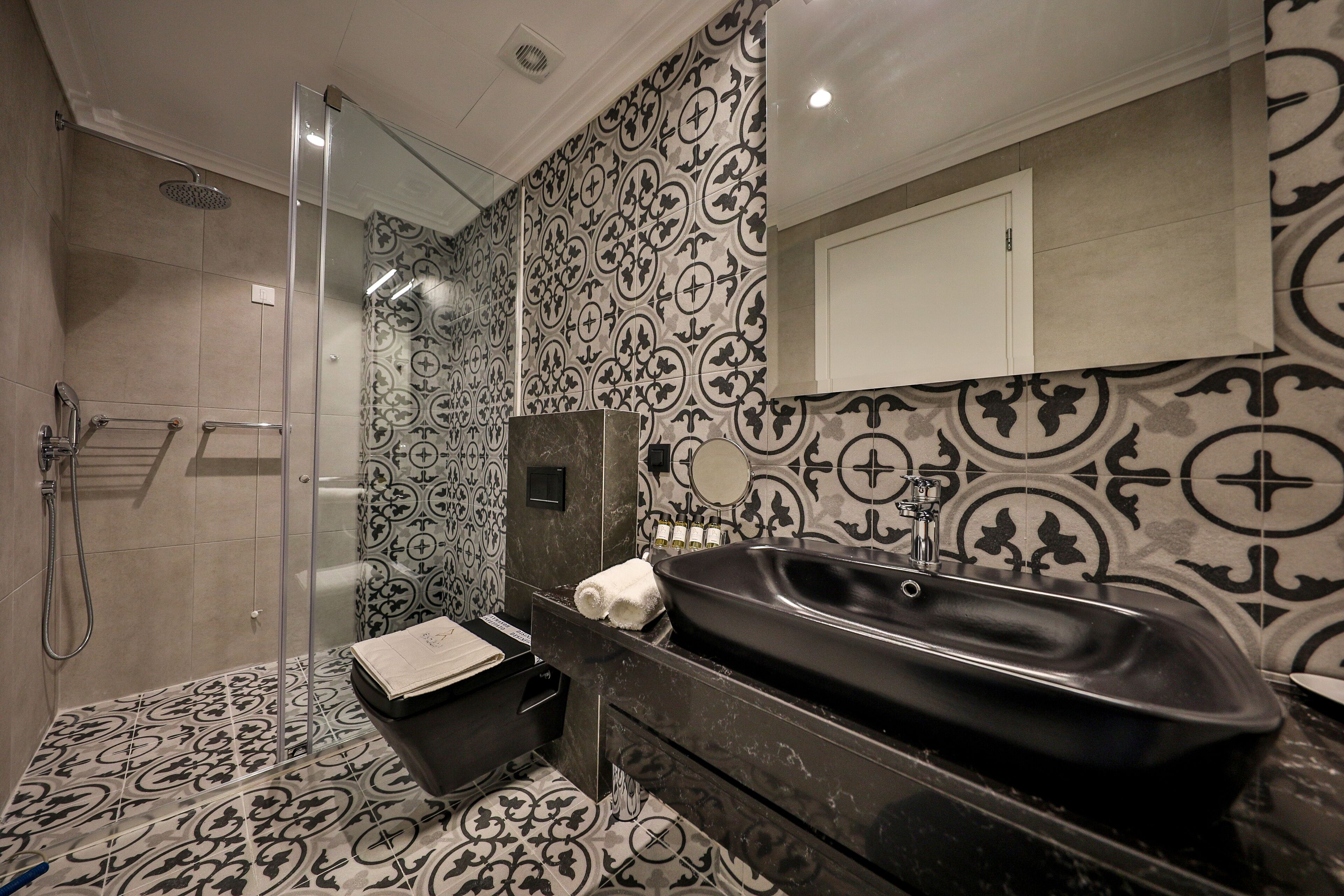 Un baño con una bañera negra, ducha con cerramiento de vidrio, azulejos estampados y un armario blanco.