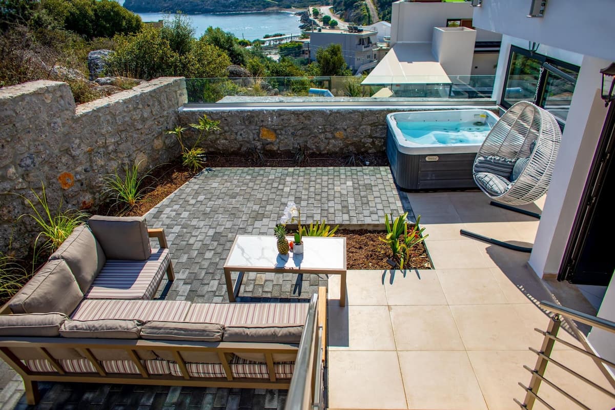 A modern outdoor patio with a hot tub, seating area, and a view of the sea.