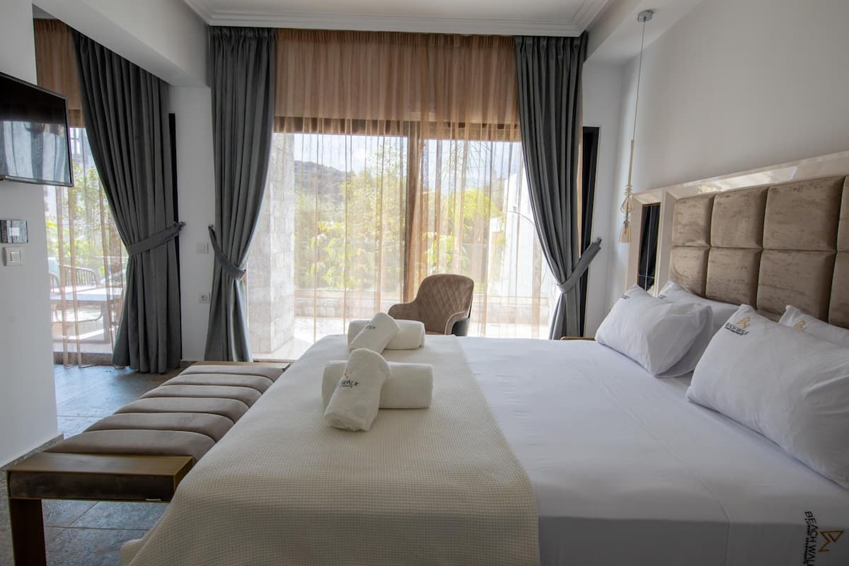 A hotel room with a large bed, a bench, a chair, and a view of the outdoors.