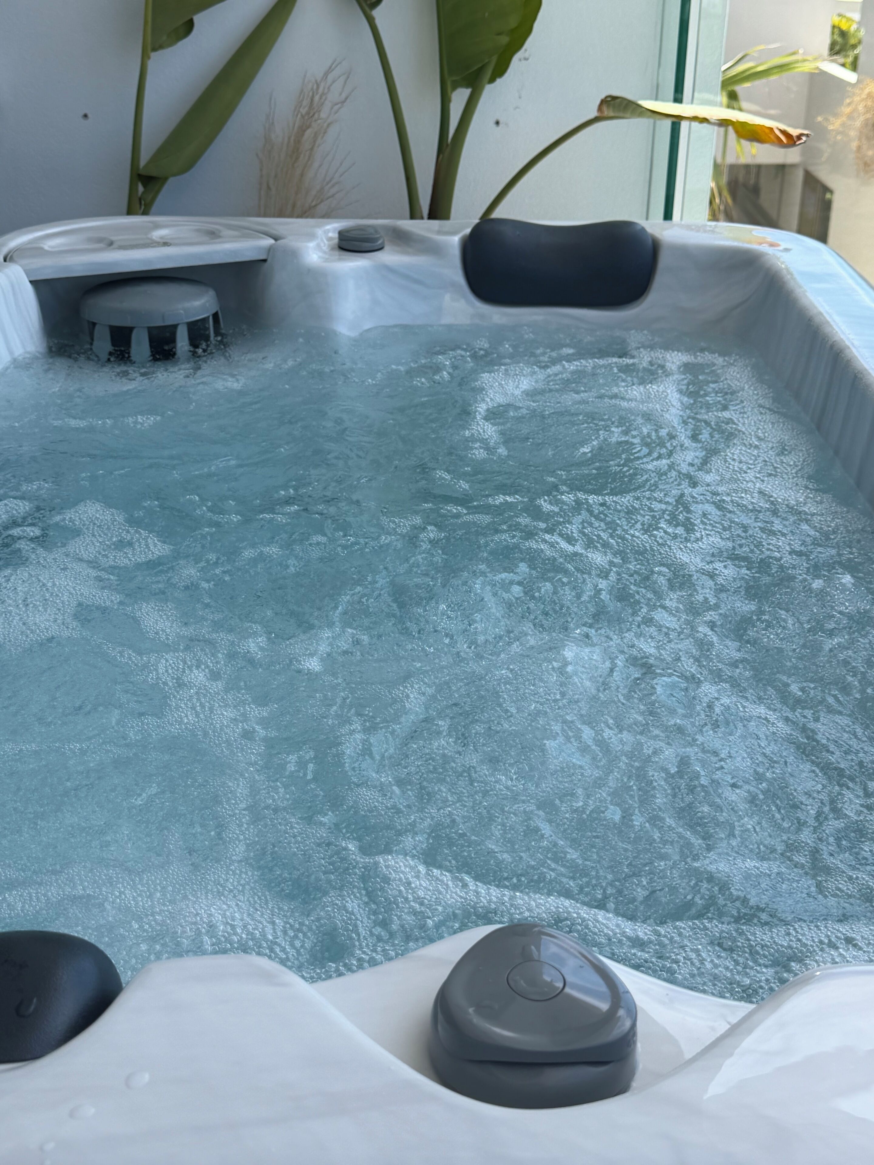 Een bubbelbad met bedieningspaneel, een klein krukje en een plant op de achtergrond.