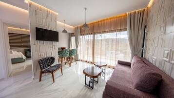 A modern living room with a sofa, a dining table, chairs, and a TV mounted on the wall.