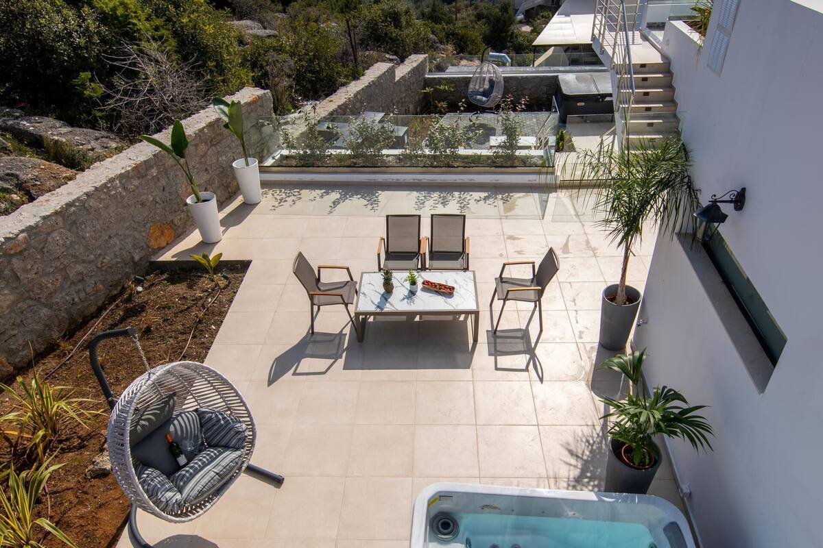 A rooftop terrace with a hot tub, outdoor seating, and a view of the sea and mountains.
