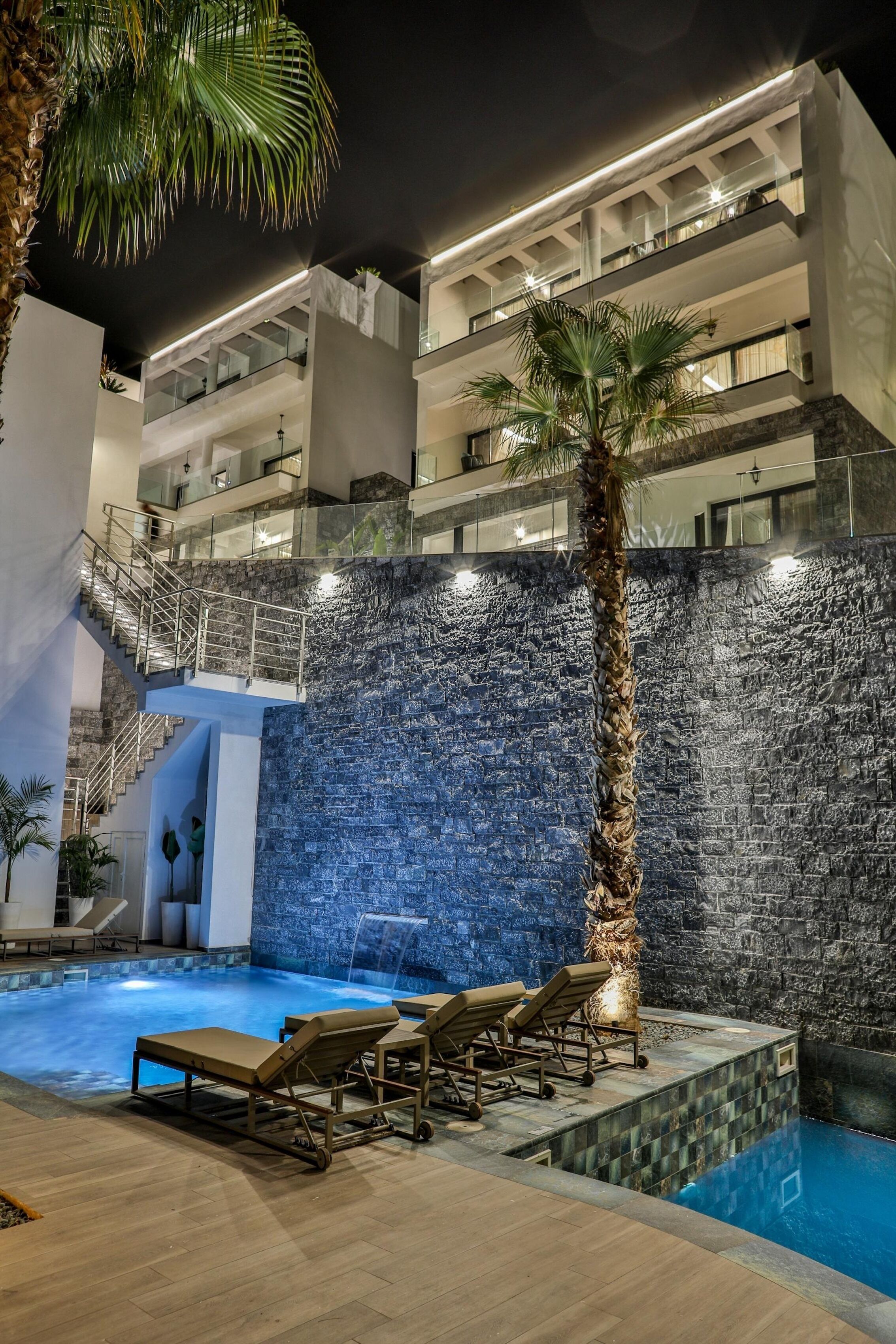 A modern hotel with a swimming pool, lounge chairs, and a palm tree.