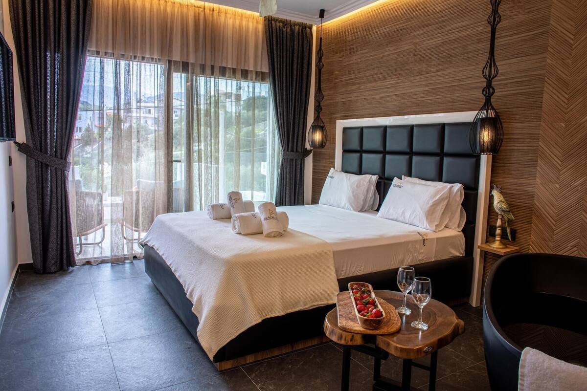 A hotel room with a bed, a small table with a fruit bowl and glasses, and a chair.