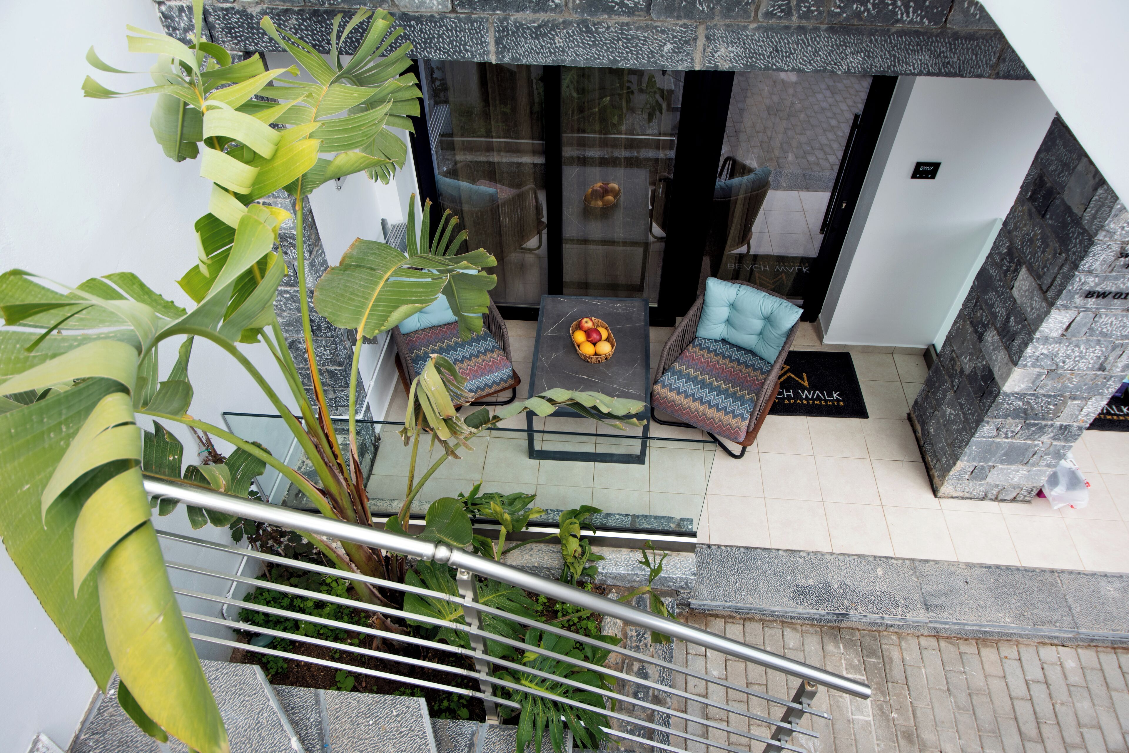 Een moderne buitenruimte met een glazen balustrade, een stenen vloer en diverse planten.