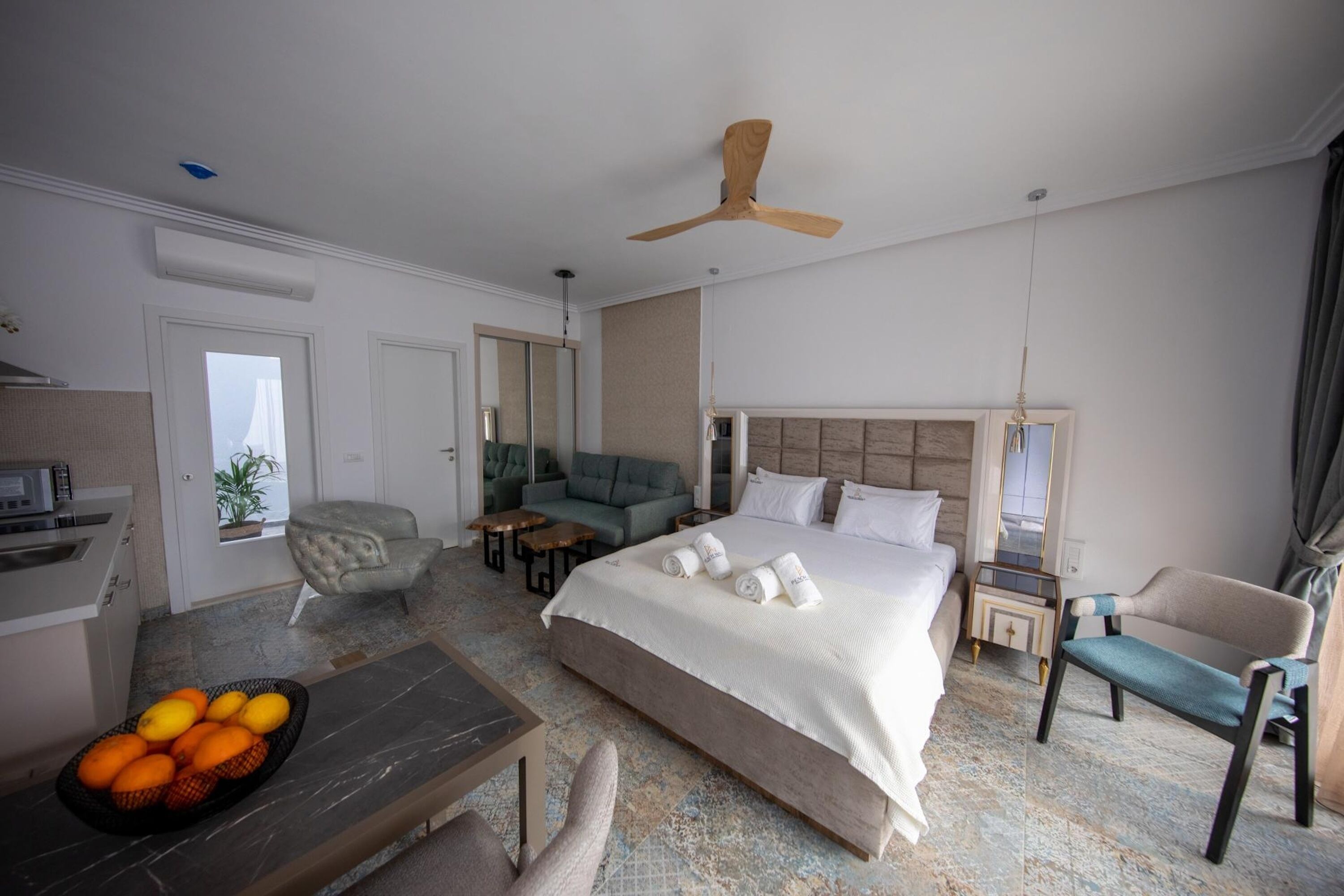Une chambre d’hôtel comprenant un lit, un canapé, une table à manger, une chaise, une petite table, un ventilateur de plafond et une fenêtre avec des rideaux.