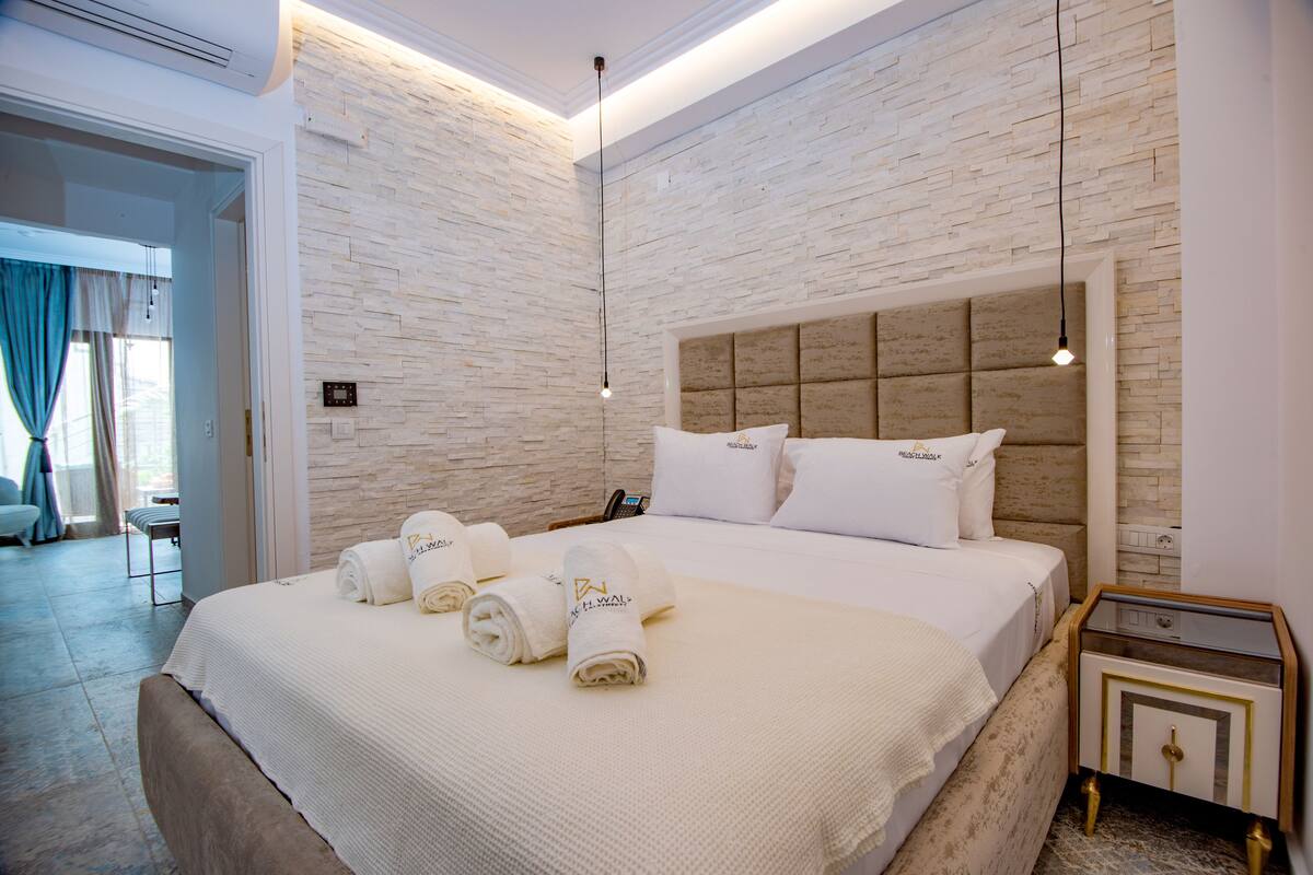 A hotel room with a large bed, a bedside table, a nightstand, and a brick-patterned wall.