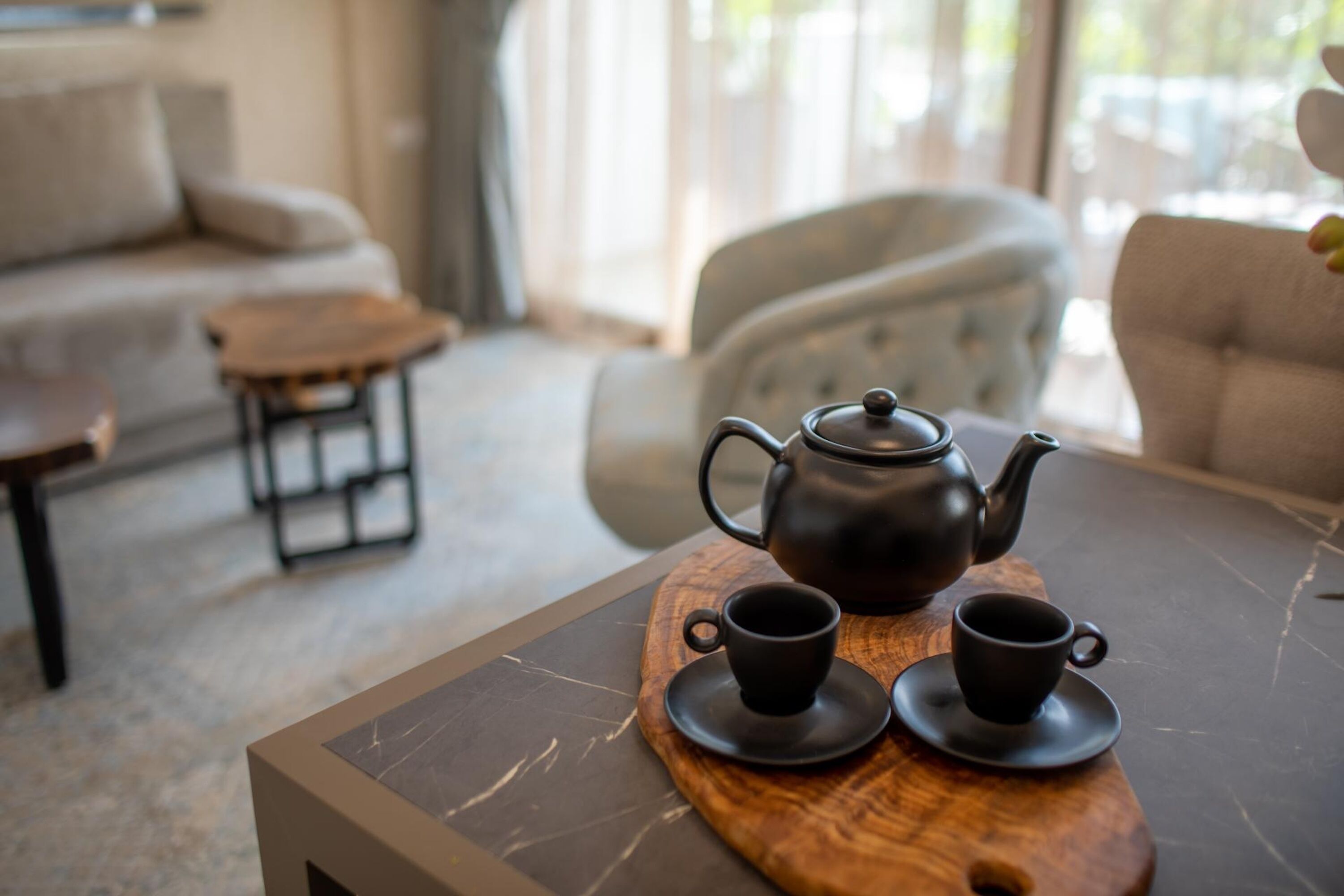 A wooden table with a teapot and two cups on a marble surface.