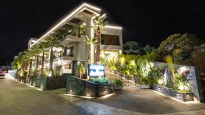 Um hotel moderno com uma entrada bem iluminada, um jardim ajardinado e uma placa indicando o nome.