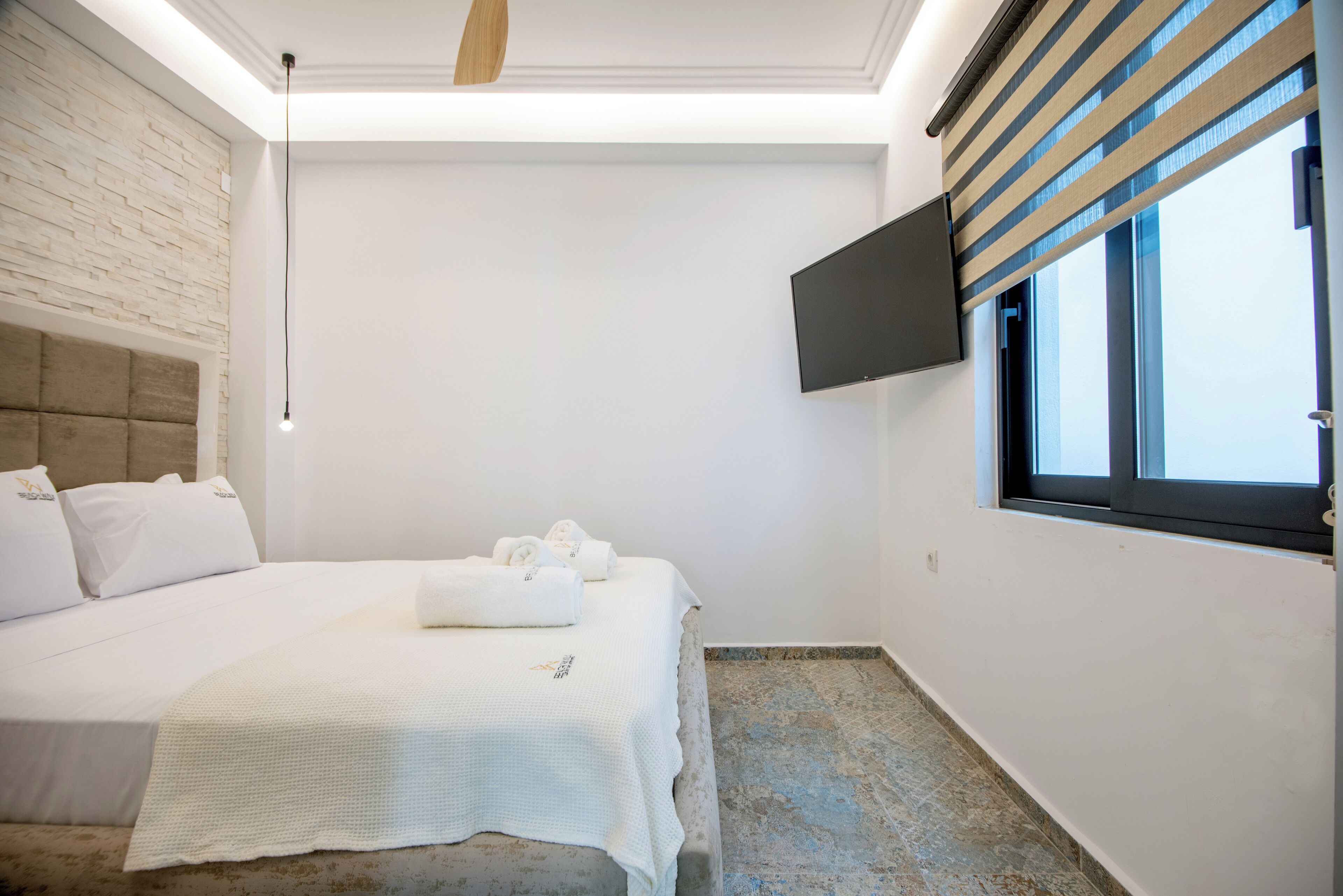 Una habitación de hotel moderna con una cama grande, un televisor de pantalla plana en la pared y una ventana con persianas.