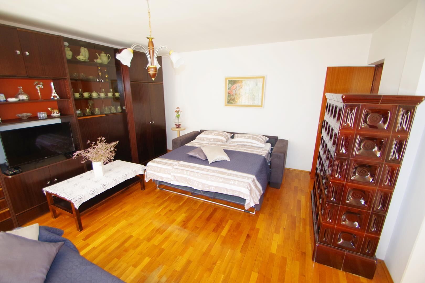 Une chambre à coucher avec un lit, une télévision, une armoire en bois et une petite table sur laquelle est posé un vase.