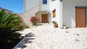 Une maison à deux étages avec un patio carrelé, un escalier en pierre et une porte en bois.