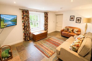 A living room with a sofa, a wooden chest, a patterned rug, a television, and a window with curtains.