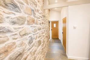A hallway with a stone wall, wooden door, and tiled floor.