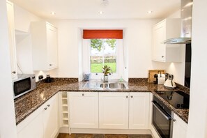 A modern kitchen with white cabinets, granite countertops, a stainless steel sink, and a built-in oven.