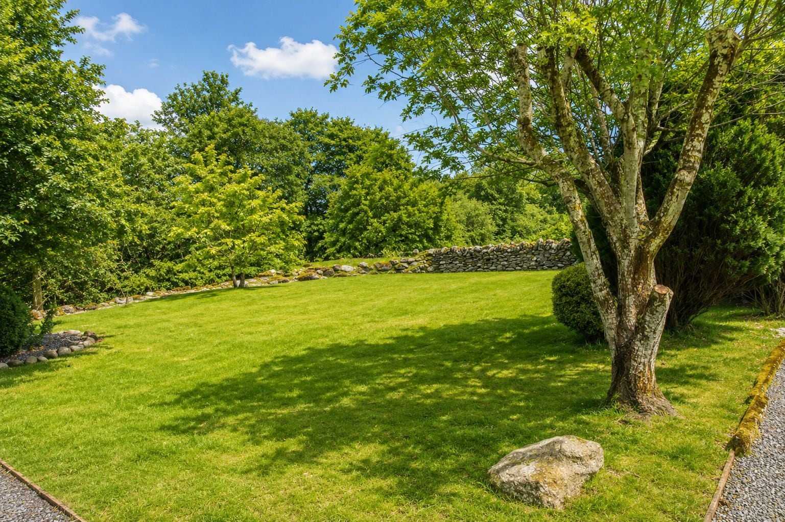 A well-maintained grassy area with a stone wall and trees.