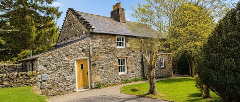 A stone house with a gravel driveway, a wooden door, and a well-maintained lawn.