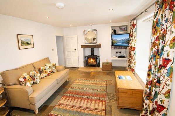 A cozy living room with a sofa, a fireplace, a television, and a patterned curtain.