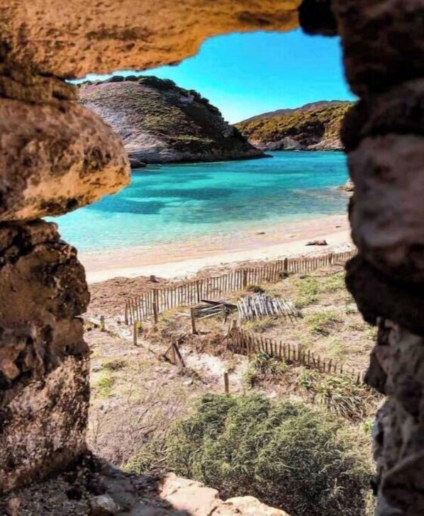 Stunning coastal view through a natural rock archway, overlooking a sandy beach and the calm sea beyond.
