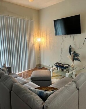 Uma sala de estar moderna com sofá, abajur, televisão de tela plana na parede e uma escultura decorativa de pena.