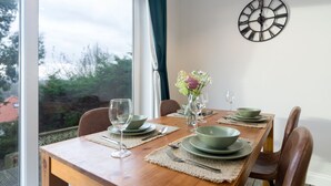 A dining table set with green plates, bowls, and cutlery, a vase with flowers, and a wall clock.