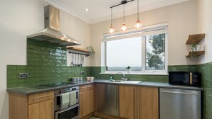 A modern kitchen with green tiles, stainless steel appliances, wooden cabinets, and pendant lighting.