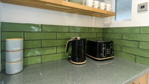 A kitchen with green tiled backsplash, a coffee maker, a toaster, and labeled containers for sugar, coffee, and tea.