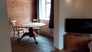 A room with a wooden dining table, two chairs, a television on a wooden cabinet, and a window with curtains. - Sycamore Lodge-1 Bed-sleeps 4-free Parking (Hereford)