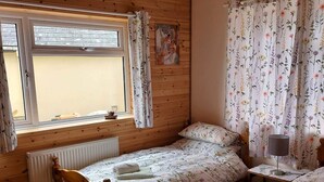 A wooden room with two single beds, a window with curtains, a radiator, and a small table with a lamp. - Sycamore Lodge-1 Bed-sleeps 4-free Parking (Hereford)