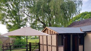 A rustic wooden building with a metal roof, a picnic table, and a fenced area with greenery. - Sycamore Lodge-1 Bed-sleeps 4-free Parking (Hereford)