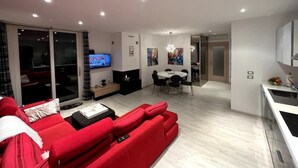 Ein modernes Wohnzimmer mit einem roten Sofa, einem Fernseher und einem Essbereich mit einer Chandelüster.