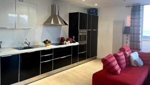 Eine moderne Küche mit schwarzen Schränken, einer Edelstahl-Dunstabzugshaube und einem roten Sofa mit gestreiften Kissen.