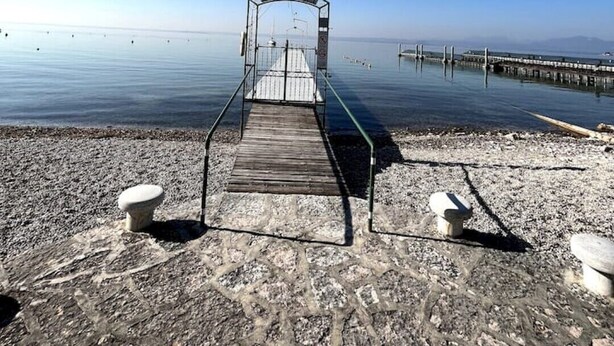 Eine Holzstege, der sich in ruhiges Wasser erstreckt, mit blauem Himmel.