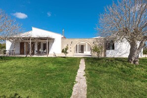 Una casa moderna con un camino empedrado que conduce a la entrada, rodeada de un césped cuidado y algunos árboles.