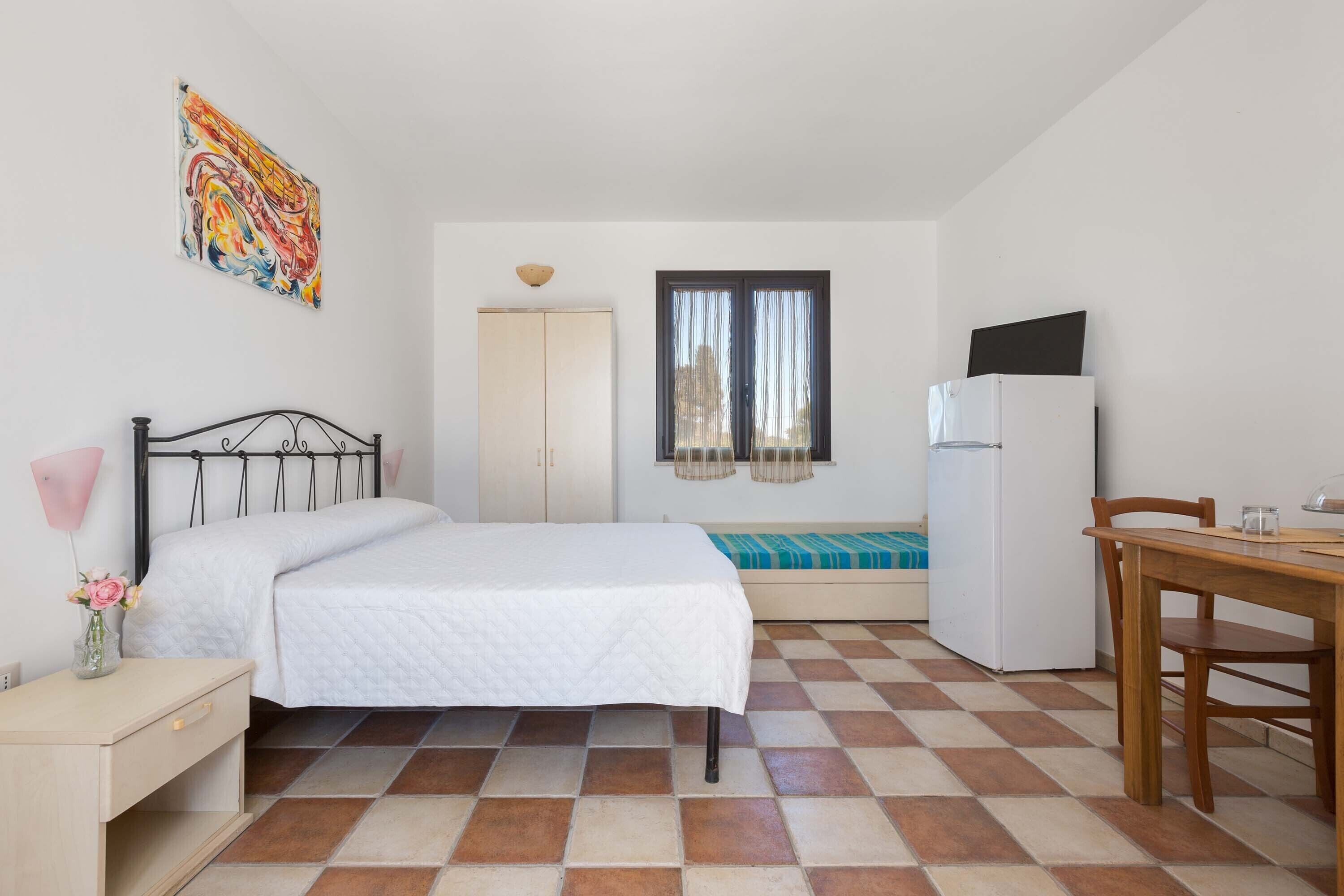 Una camera da letto con un letto, una scrivania, una sedia, un frigorifero e una finestra con tende.