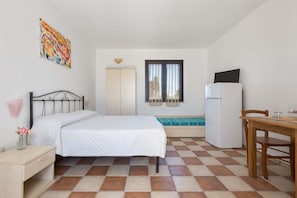 Un dormitorio con cama, escritorio, silla, refrigerador y ventana con cortinas.