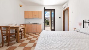 Un dormitorio con una cama, un escritorio de madera y una zona de cocina con armarios.