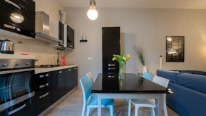 A modern kitchen with black cabinets, a stainless steel stove, and a dining table with blue chairs.