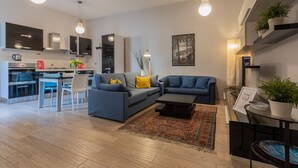 A modern living room with a grey sofa, a coffee table, and a kitchen area with a dining table and chairs.