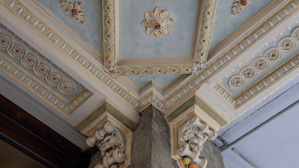 A ceiling with intricate floral and geometric patterns, a stone column with a carved figure, and a partially visible wooden structure. - La Maison du Vent by Wonderful Italy (Torino)