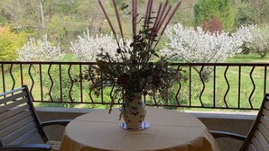 A round table with a white tablecloth, a vase with flowers, and two wooden chairs on a balcony with a view of blooming trees. - Gîte Studio with Balcony in Venasque (Venasque)