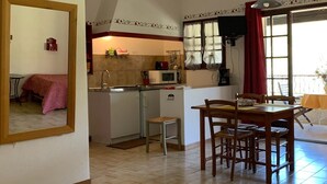 A compact kitchen with a dining area, a small stool, and a table with chairs. - Gîte Studio with Balcony in Venasque (Venasque)