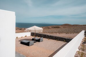 Una terraza en la azotea con un muro blanco, una sombrilla blanca y cojines negros.