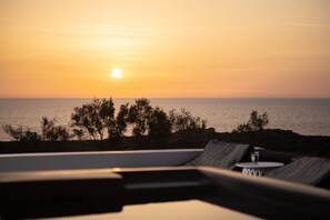 Vista al atardecer desde un balcón con piscina, sillones de descanso y una pequeña mesa.
