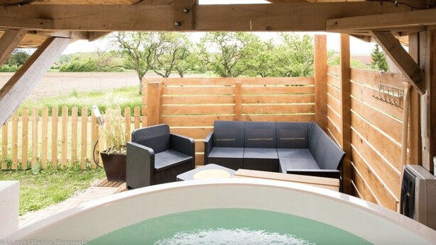 Eine Holzterrasse mit Whirlpool, zwei schwarzen Korbstühlen und einem Holzzaun.