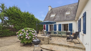 A stone patio with outdoor seating, a grill, and a potted hydrangea bush. - 800 m from harbour – House terrace BBQ – Sleeps 12 (Loctudy)