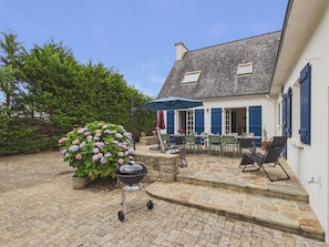 A stone patio with outdoor seating, a grill, and a potted hydrangea bush.
